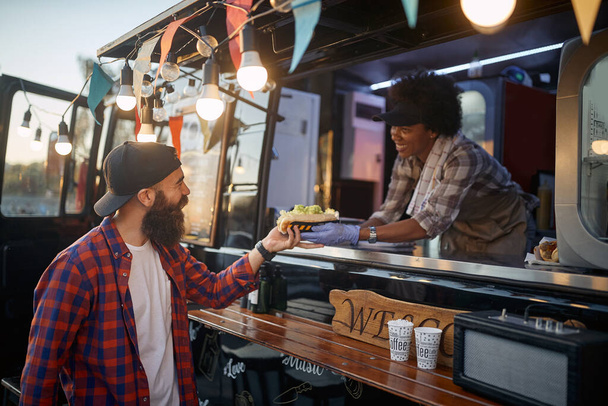 young beardy hipster taking sandwich to go from polite female employee in fast food service - 写真・画像