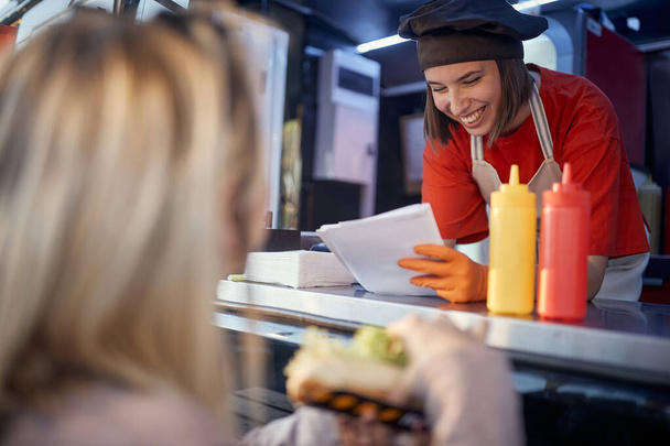 beautiful young caucasian female employee in fast food service writing down on a paper customer suggestion with a big smile - Fotografie, Obrázek