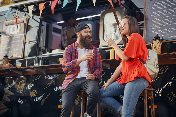 young caucasian couple talking, smiling, drinking in front of modified truck for fast food service - Fotografie, Obrázek
