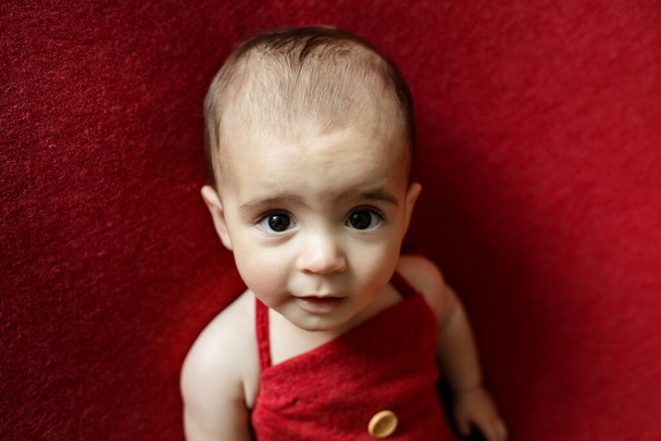 Мила новонароджена дитина. Щаслива дитина на червоному тлі. Портрет новонародженої дитини крупним планом. Шаблон упаковки дитячих товарів. Розплідник. Медична та здорова концепція. Різдво. Новий рік
 - Фото, зображення