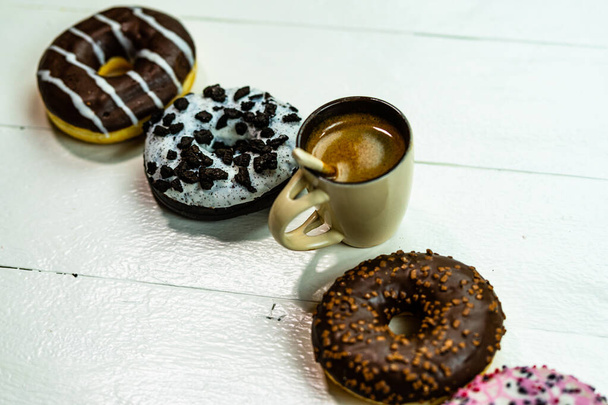 Bunte Donuts und Kaffeetasse auf weißem Holztisch. Süße Bäckerei mit glasierten Streusel, Frühstückskonzept. Draufsicht mit Kopierraum - Foto, Bild
