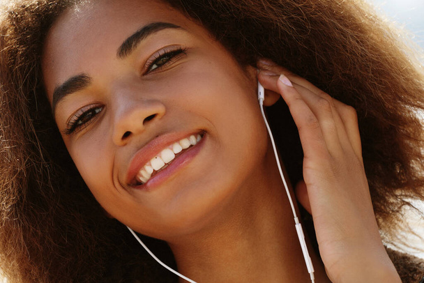 Young african american girl using mobile phone and headphones, smiling, close up - Foto, Imagen