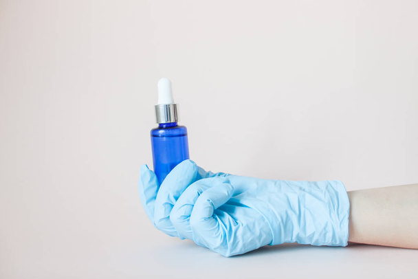 Bottles with serum for the face in his hands in protective medical rubber gloves on a light background. Beauty industry. - Photo, image