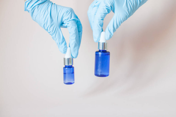 Bottles with serum for the face in his hands in protective medical rubber gloves on a light background. Beauty industry. - Photo, image