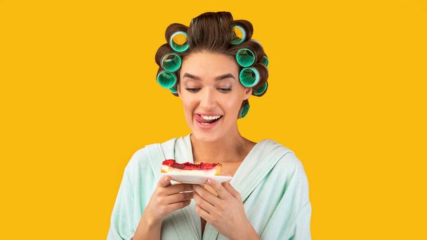 Hambrienta ama de casa en una dieta sosteniendo pastel sobre fondo amarillo - Foto, Imagen