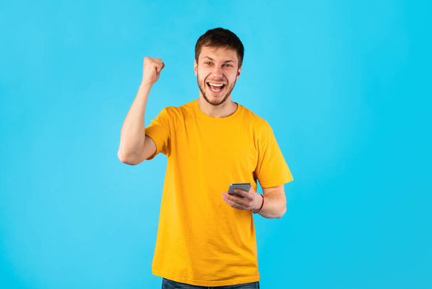Захоплений чоловік використовує мобільний телефон на студії, святкуючи перемогу
 - Фото, зображення