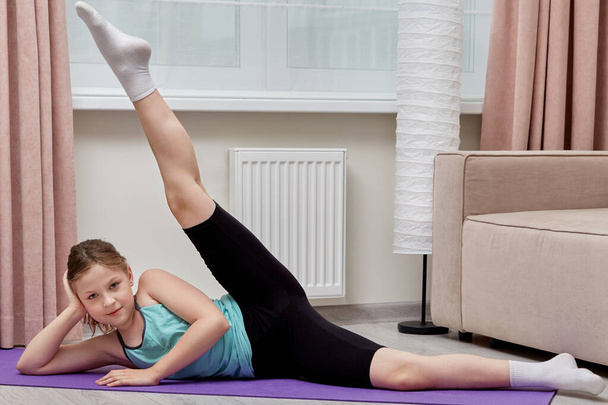 The girl performs sports exercises at home for flexibility. Leg raised up. - 写真・画像