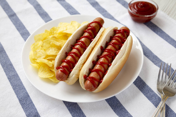 Вкусный американский Hot Dog с картофельными чипсами на белой тарелке, вид под низким углом.  - Фото, изображение