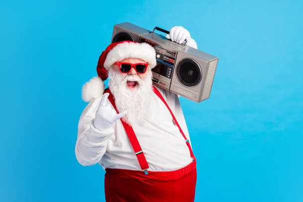 Photo of cool stylish modern white grey hair bearded santa claus listen x-mas christmas music boom box show horned symbol wear red suspenders overalls isolated blue color background - Photo, image