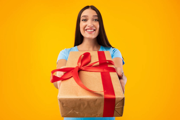 Happy woman holding gift box at studio, giving to camera - Photo, Image