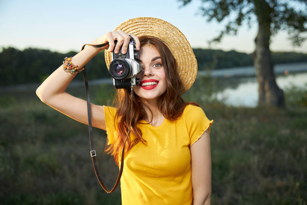 Woman holding camera looks into the camera lens red lips hat nature  - Foto, immagini