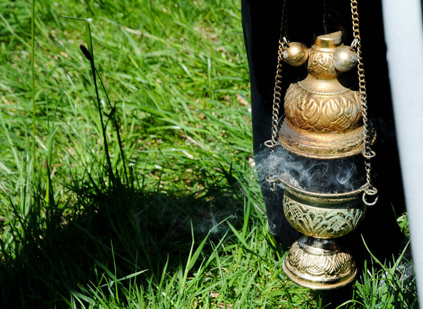 Zbliżenie posiadacza kadzidła do tradycyjnego ortodoksyjnego rytuału, z dymem palącego się kadzidła, na zewnątrz z zieloną trawą jako tłem - Zdjęcie, obraz
