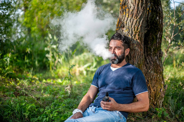 Fumatore fiducioso soffiando un sacco di fumo utilizzando vaporizzatore elettronico dispositivo di fumo. Modi moderni di smettere di fumare. - Foto, immagini