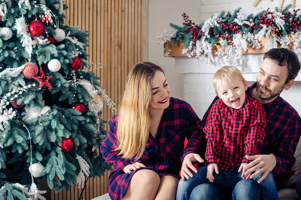 Happy family in Christmas time near the Christmas tree. Young mother and father with their son. - Foto, Bild