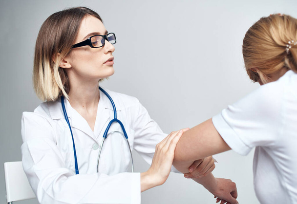 médico examina o paciente dobrando o braço em um fundo leve e um estetoscópio - Foto, Imagem