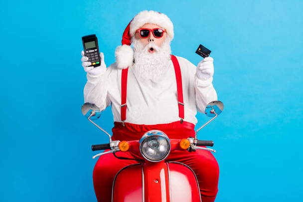 Photo of grandfather grey beard ride retro moped hold demonstrate debit card terminal wear santa claus x-mas costume suspenders sunglass white shirt cap isolated blue color background - Fotografie, Obrázek