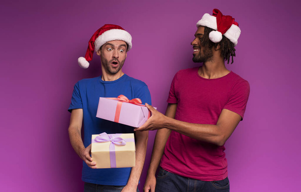 Amazed friends happy by the arrival of Christmas with present. Purple background - Photo, image