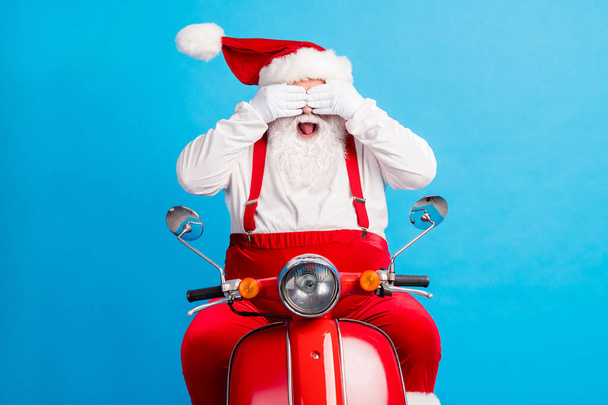 Photo of excited santa claus ride scooter x-mas magic surprise christmas stylish modern party close cover hands eyes wear style trendy hat suspenders overall isolated blue color background - Photo, Image