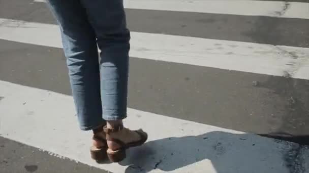 Веселая молодая девушка в летней одежде и туфлях прыгает по дороге вдоль белых линий пешеходного перехода. Крупные ноги. - Кадры, видео