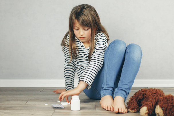 Psicológico, salud mental. Una adolescente se sienta en el suelo y le echa pastillas en la mano. Ayuda para adolescentes. Copiar espacio. - Foto, imagen