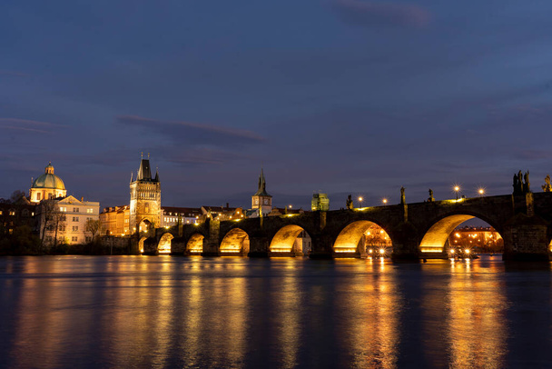 old monument charles bridge from 14 century built of stone and statues and street lights at night on the river in ltava in the center of prague in czech republic - Photo, Image