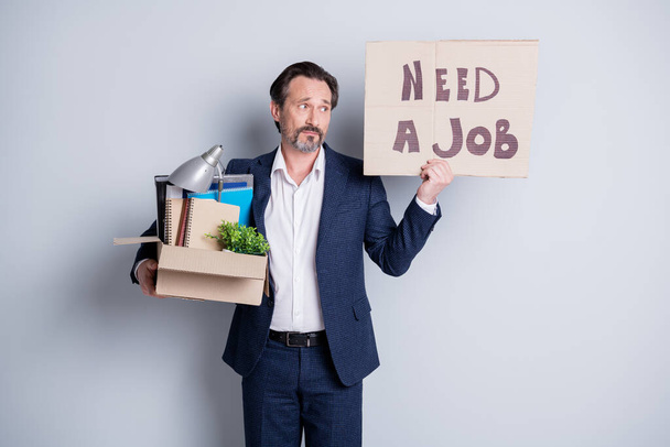 Looking for a job. Photo of unhappy worker mature guy financial crisis lost work hold carton box belongings quit hold placard banner search work place wear suit isolated grey background - Фото, изображение