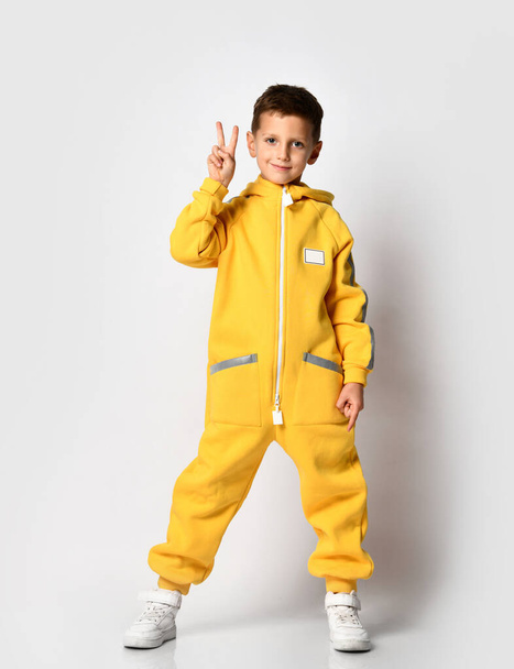 Boy in yellow warm jumpsuit showing victory gesture - Photo, image