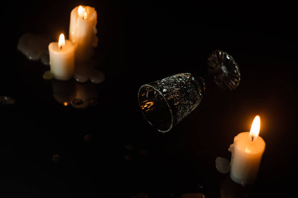 Vaso de cristal volcado tendido sobre una mesa de espejo oscuro entre velas. Concepto de fiesta o celebración - Foto, Imagen