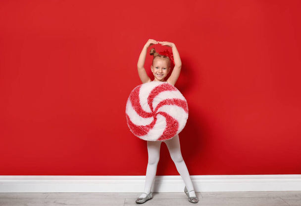 Cute little girl dressed as candy near red wall. Christmas suit - Valokuva, kuva