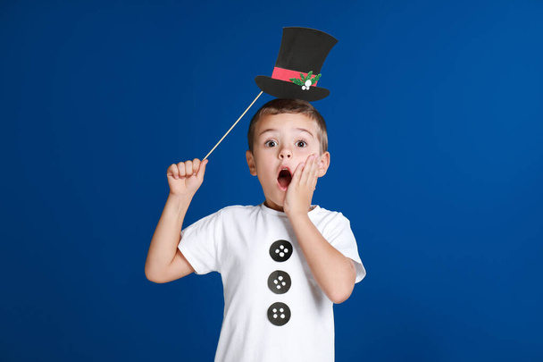 Shocked little boy with Christmas hat prop on blue background - Photo, Image