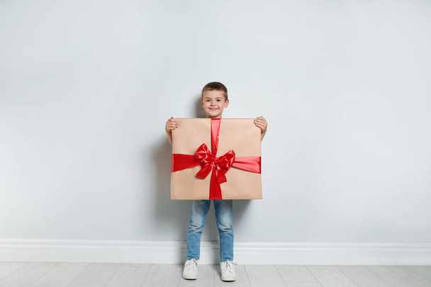 Cute little boy dressed as gift box near white wall. Christmas suit - Φωτογραφία, εικόνα