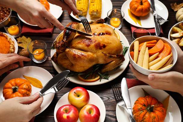 People eating traditional cooked turkey at wooden table, closeup. Thanksgiving day celebration - 写真・画像