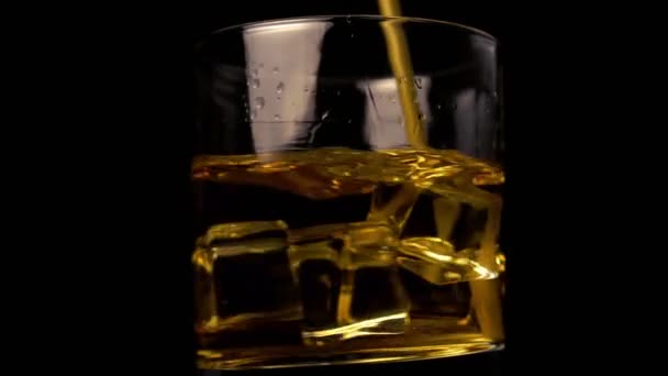 Golden Whiskey on a black background with ice cubes. Drinking straw stir the drink. Splash drops. Base rotation - Imágenes, Vídeo