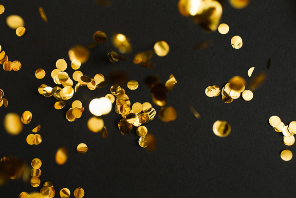 Golden confetti on black background. Festive holiday backdrop. Birthday congratulations Christmas New Year. Flat lay, top view, copy space. selective focus - Фото, зображення