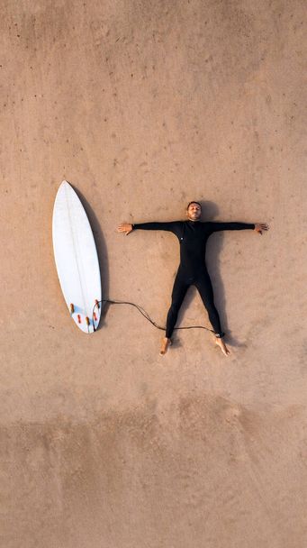 Sörf yapmayı seviyorum. Dalgıç kıyafetli bir sörfçünün sahilde kumsalda yatan sörf tahtasının en üst görüntüsü. Sörf okulunda eğleniyorum. Yüksek kalite fotoğraf - Fotoğraf, Görsel