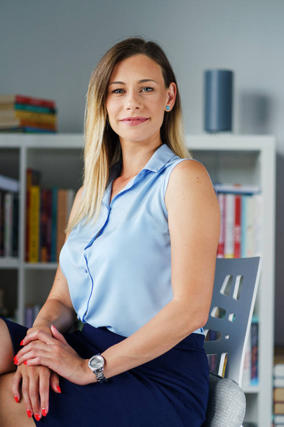 Porträt einer selbstbewussten erfolgreichen erwachsenen kaukasischen Geschäftsfrau, die zu Hause oder im Büro auf einem Stuhl vor dem Bücherregal sitzt und in die Kamera blickt - Konzept echter Menschen - Foto, Bild