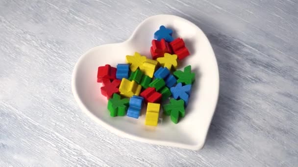 Figuras de madera multicolores juguetes en un plato blanco en forma de corazón en una pizarra. Rotación. 4K. Primer plano - Imágenes, Vídeo