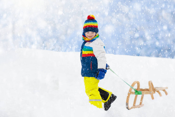 A kisfiú élvezi a szánkózást. Gyerek szánkózás. A kisgyerek szánon lovagol. A gyerekek kint játszanak a hóban. Gyerekek szánkóznak az Alpokban télen. Kültéri szórakozás családi karácsonyi vakáció. - Fotó, kép