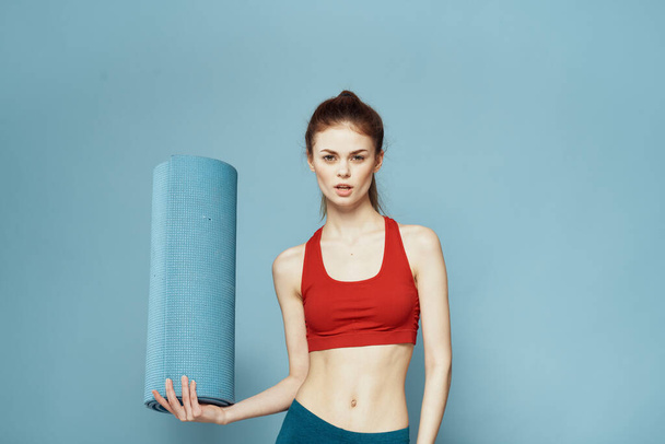 athletische Frau mit Fitnessmattenübung schlanke Figur rotes T-Shirt blauer Hintergrund - Foto, Bild