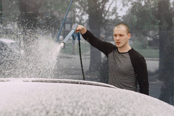 Handsomen man in a black sweater washing his car - 写真・画像
