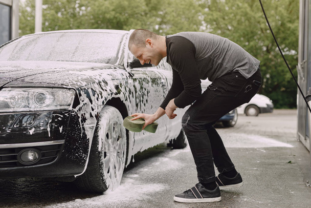 Handsomen man in a black sweater washing his car - Fotoğraf, Görsel