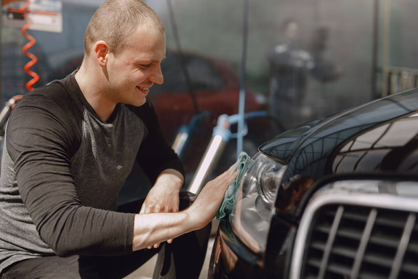 Man in a gray sweater wipes a car in a car wash - Fotoğraf, Görsel