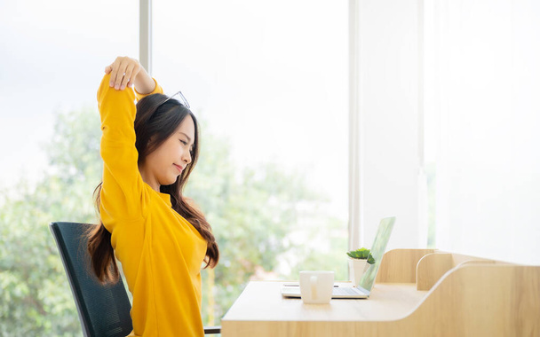 Концепция офисного синдрома. Молодая азиатская женщина чувствует боль в шее и плече после долгой работы на компьютере ноутбуке. Она растягивается, чтобы расслабить мышцы - Фото, изображение