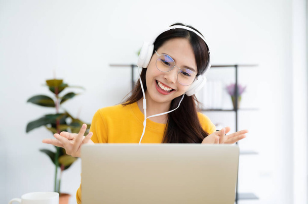 Young asian woman in headphone having conversation chatting while using laptop at house. Work at home, Video conference, Online meeting video call, Virtual meetings, Remote learning and E-learning - Photo, Image
