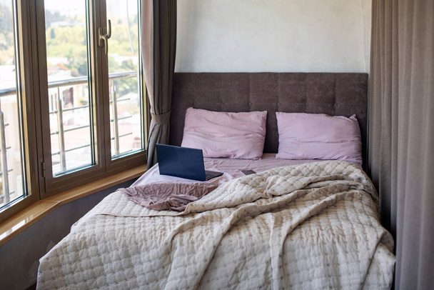 Doppelbett mit Pastellbettwäsche. Laptop im Bett. Arbeiten und spielen Sie mit einem Laptop, während Sie im Bett liegen. Morgen in der Wohnung - Foto, Bild