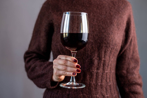 Eine Frau im braunen Pullover hält ein Glas Rotwein in der Hand. Nahaufnahme. - Foto, Bild