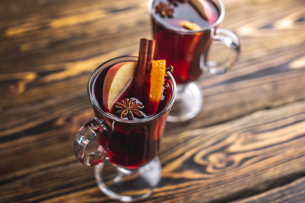 Couple glass cups with mulled wine decorated with cinnamon, star anise and fruit on a wooden table. Concept of a traditional hot winter beverage. - Foto, Imagen