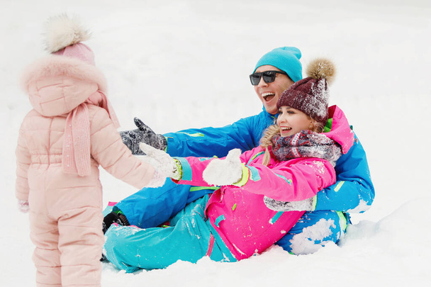 Familia mamá, papá e hija revolcarse y divertirse en la nieve blanca en el parque de invierno. Enfoque selectivo, fondo borroso. - Foto, imagen