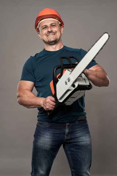 Caucasian worker in hardhat holding a new chainsaw - Foto, Imagen