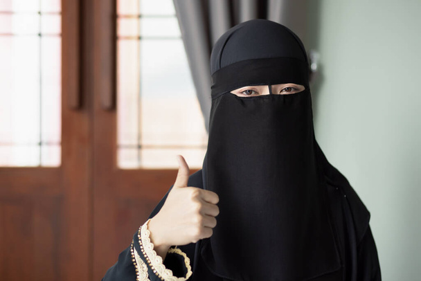 Bliskowschodnia muzułmanka z zasłoną na twarzy wskazującą na gest aprobaty. - Zdjęcie, obraz